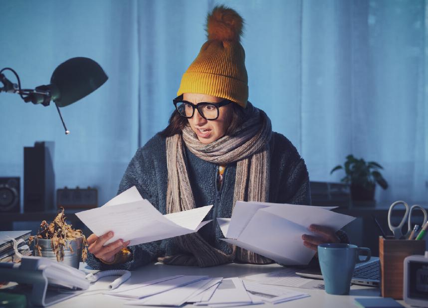 Woman bundled in winter clothing reviewing heating bills indoors, representing comparison of electric vs gas heating costs