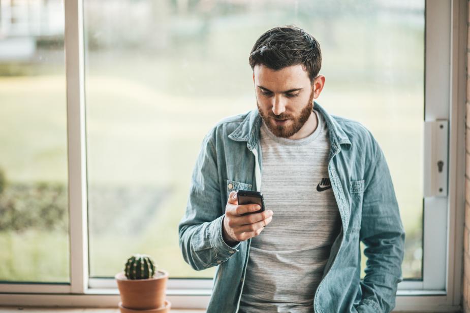A man staring at his phone near a window. 